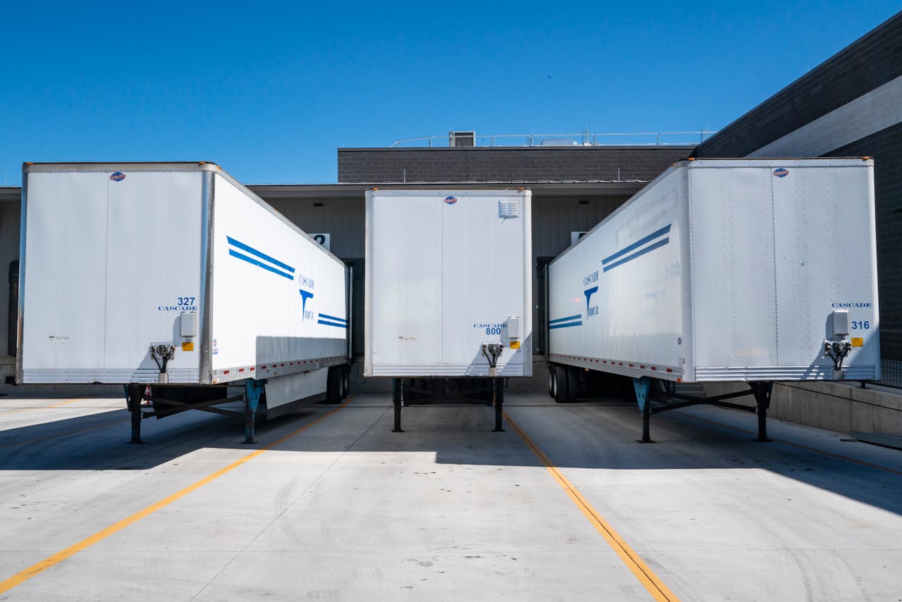 services-01 Three white cargo trailers parked at an industrial shipping dock under clear blue skies.