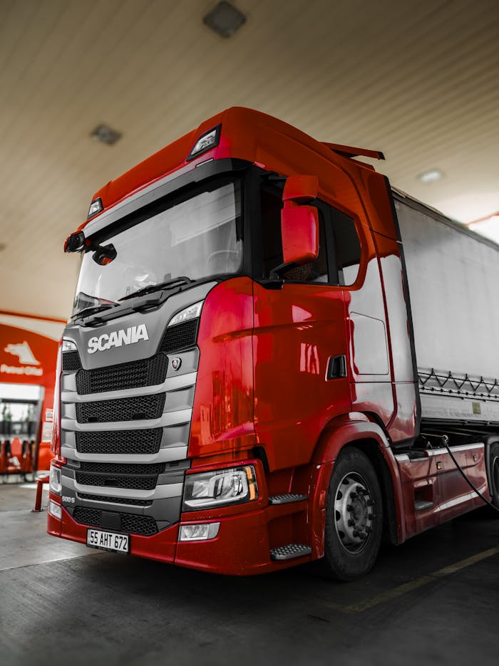 why-choose-us Bright red Scania truck parked at a fuel station with modern design and clean lines.